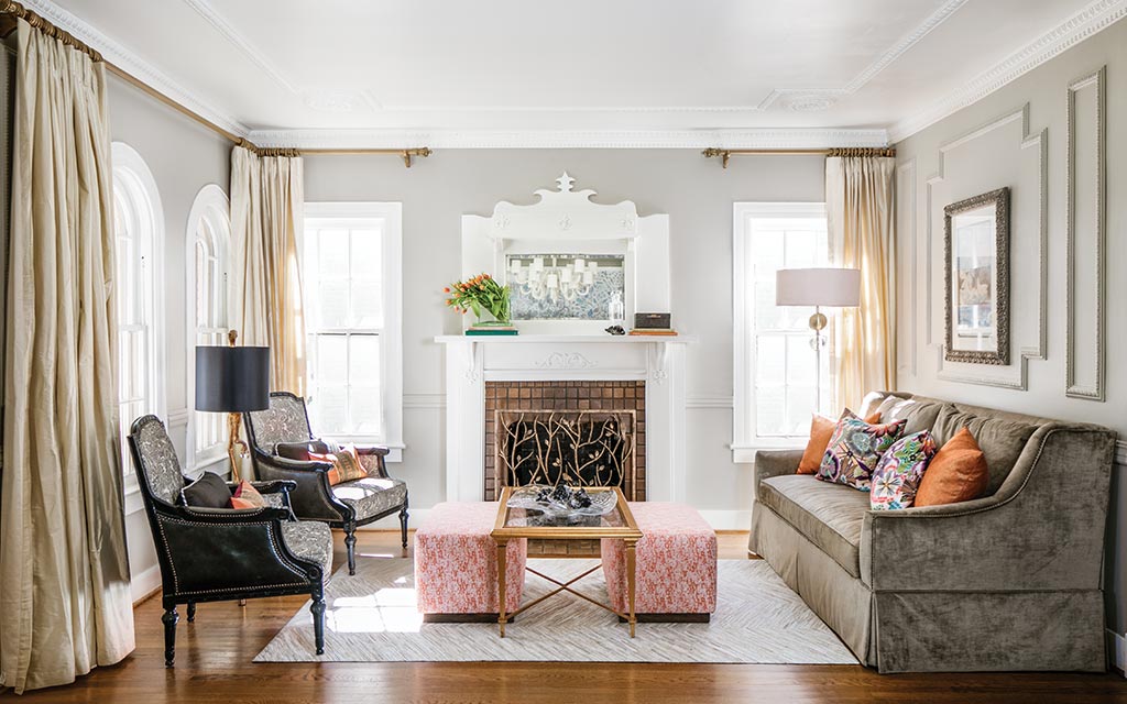 Texas renovation living room with a white fireplace, brown velvet sofa, orange ottomans, and hardwood floors