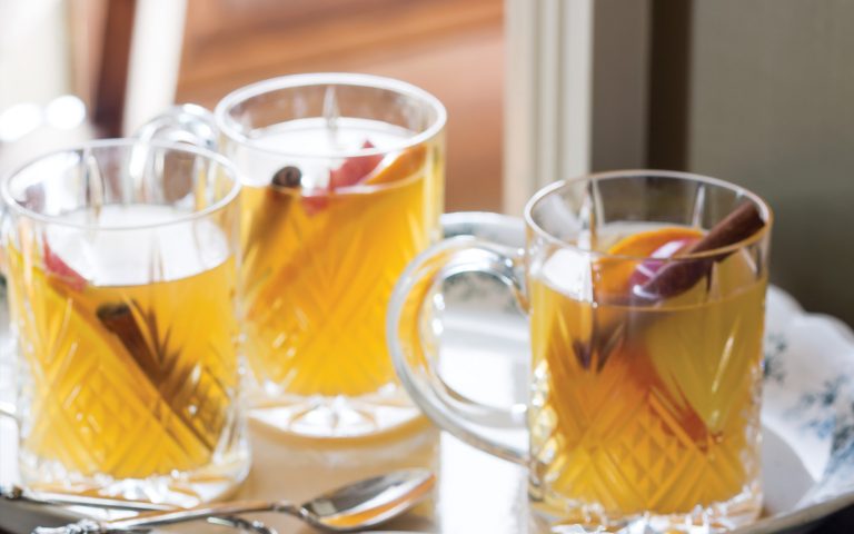 Bourbon-Maple Cider in clear glass mugs garnished with cinnamon sticks and orange slices