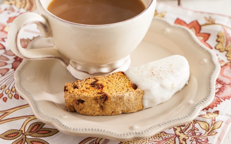 Pumpkin Spice Biscotti dipped in white chocolate on a saucer with coffee