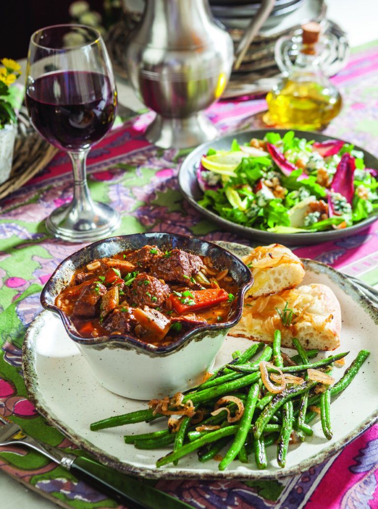 A bowl of Hearty Beef and Barley Stew with a side of green beans and carmelized onion foccacia.