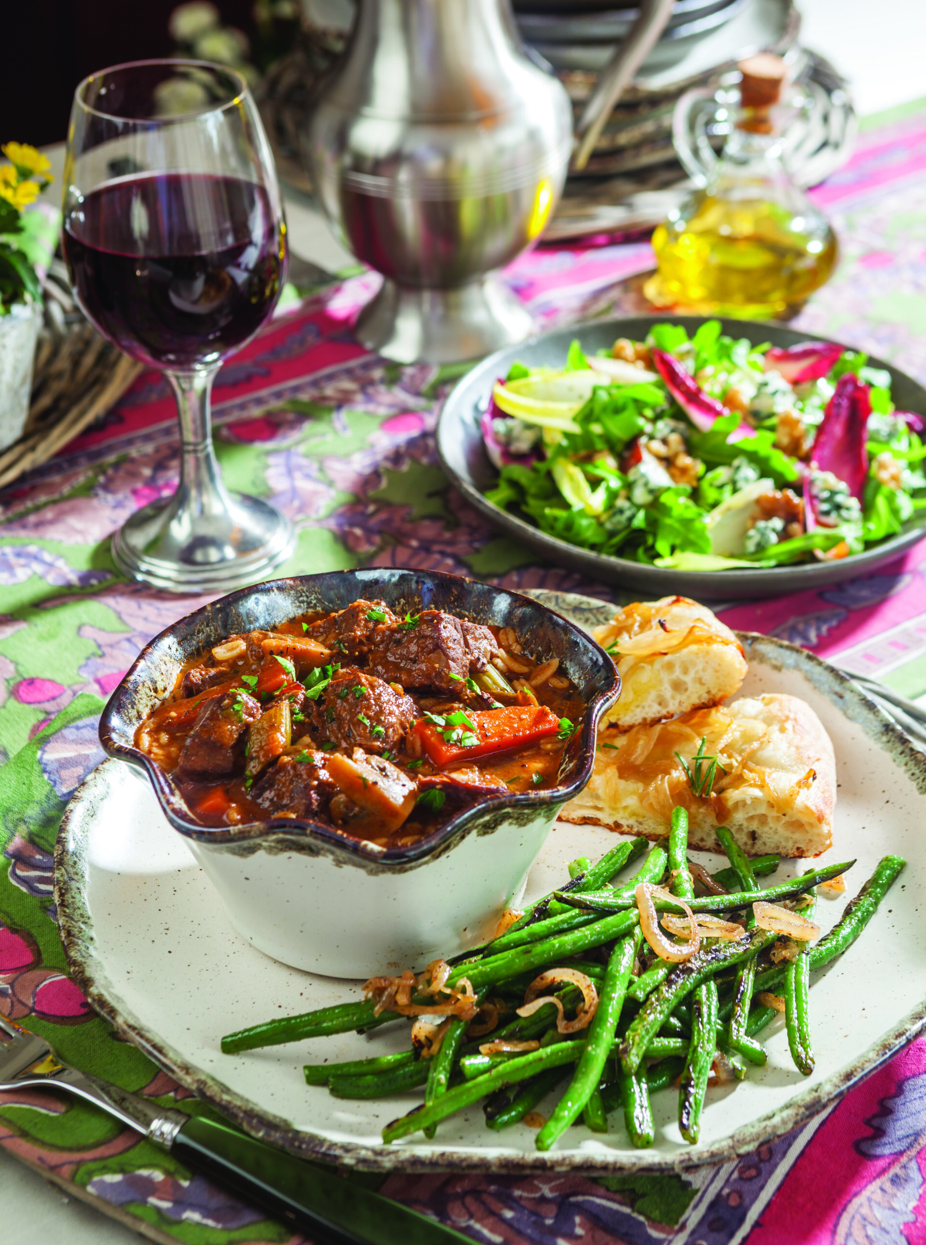A bowl of Hearty Beef and Barley Stew with a side of green beans and carmelized onion foccacia.