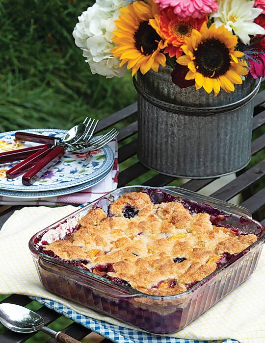 Cobbler in a glass dish with sunflowers and pink blooms behind it