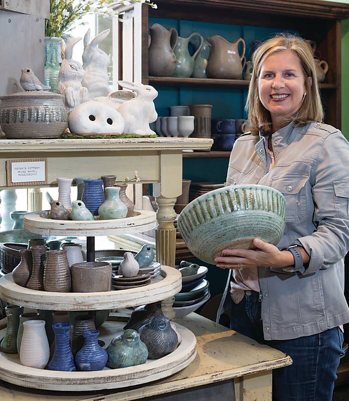 A woman holding a ceramic bowl next to a display of Mississippi-made pottery at The Mississippi Gift Company