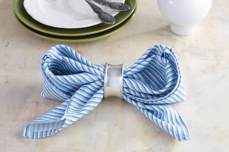 Bow Napkin Fold How-To: Blue-and-white striped napkin folded into a bow with silver napkin ring