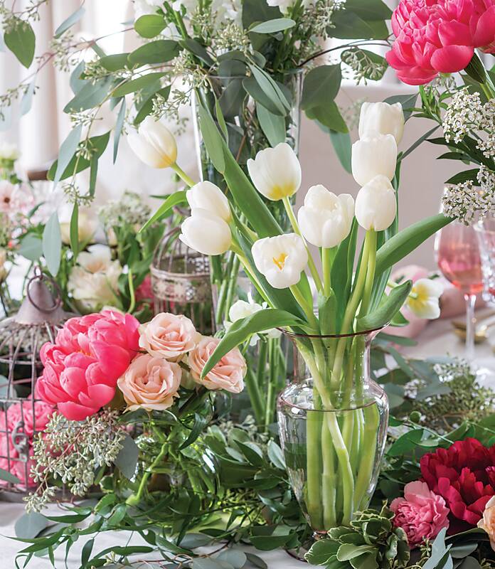 White tulips in a vase surrounded by pink roses and peonies