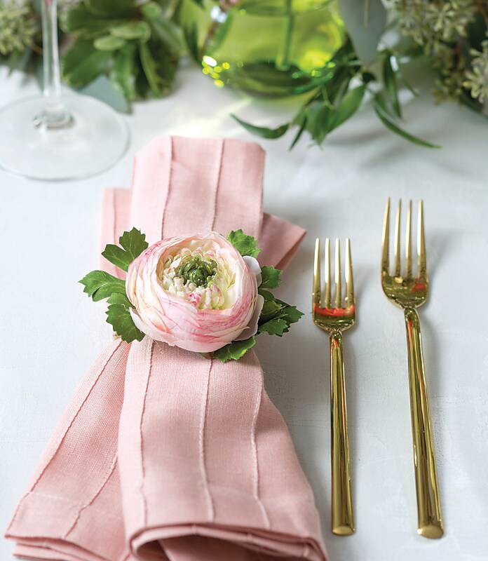 A pale pink napkin in a flower-bud napkin ring next to gold flatware