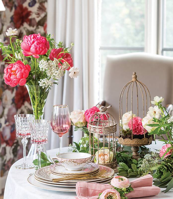 Pink and white flowers, crystal wineglasses, and stacked china next to decorative bird cages