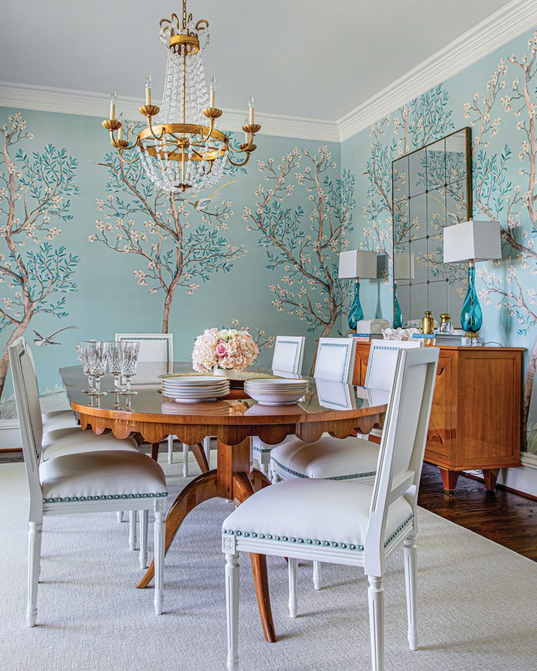 Dining room with blue garden-motif wallpaper, light wood polished table and buffet, beaded chandelier and white chairs