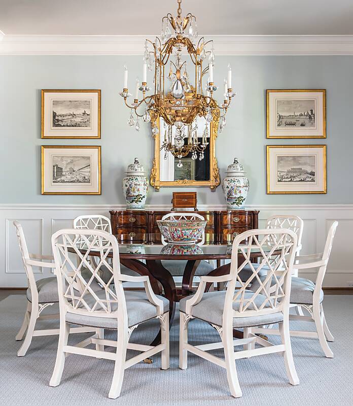 Dining room with cream chairs, dark table, gilded chandelier and mirror