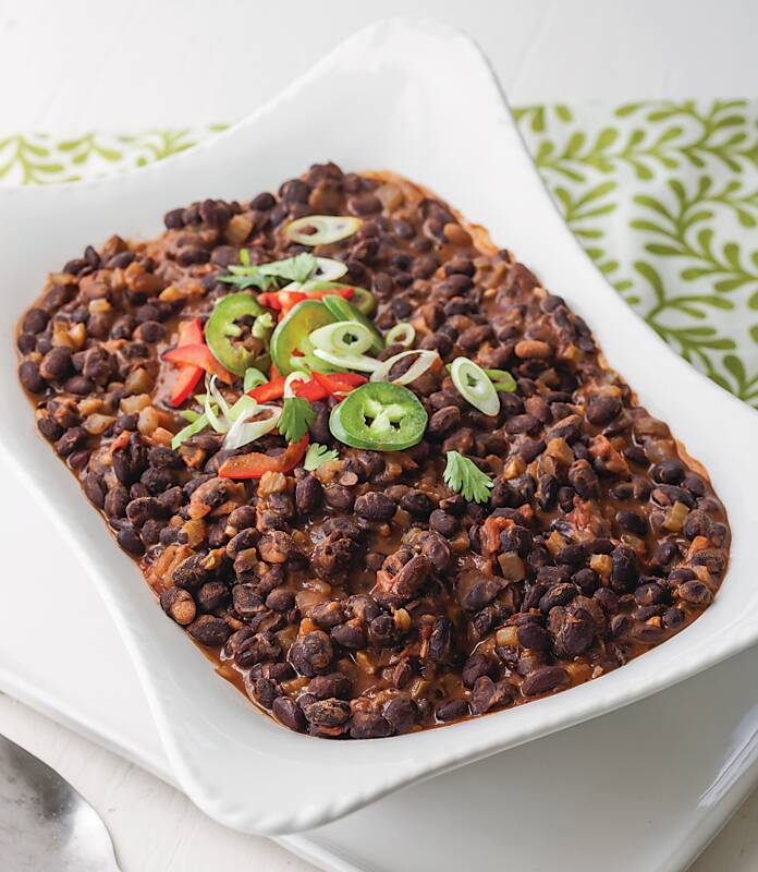 Black beans topped with sliced jalapeños in a white rectangular dish 