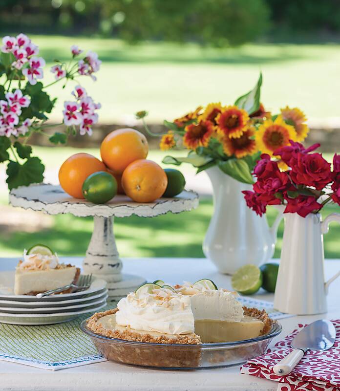 Key lime pie in a clear dish surrounded by flowers and fruit