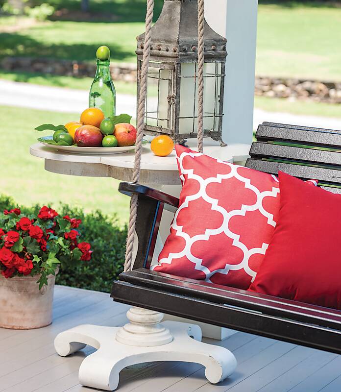A wooden porch swing topped with red throw pillows