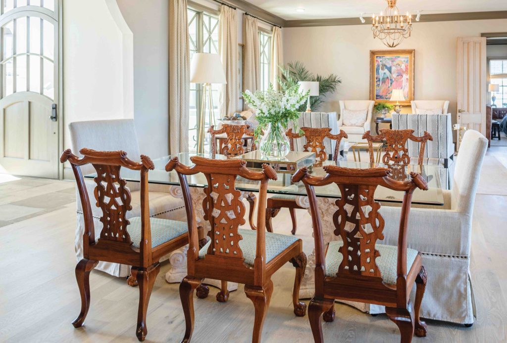 A dining room with a glass top table, wooden chairs, and upholstered host chairs
