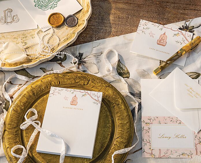 Assorted bespoke stationery, wax seals, ribbon, and a strand of pearls atop antiqued trays