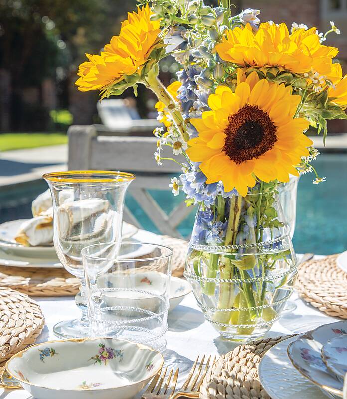 Sunflowers and blue delphinium in a clear vase amid white floral china and clear glassware