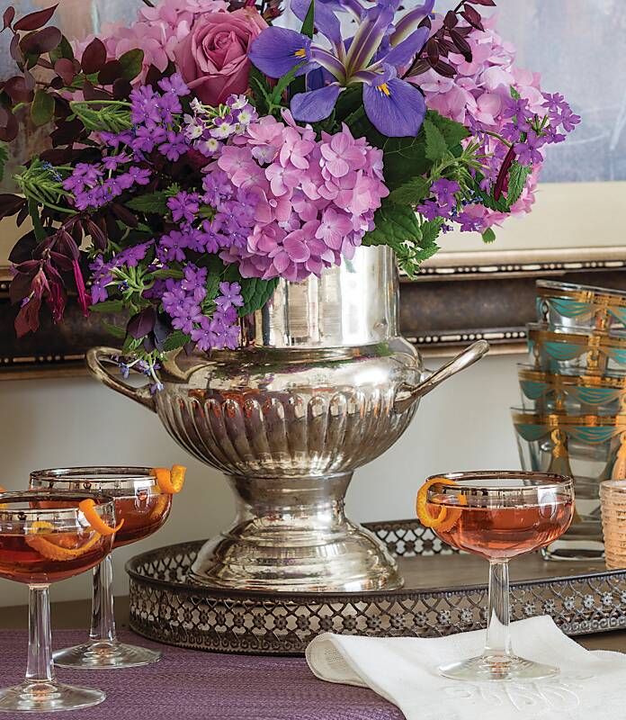 A silver urn filled with purple and pink flowers surrounded by glasses of Champagne