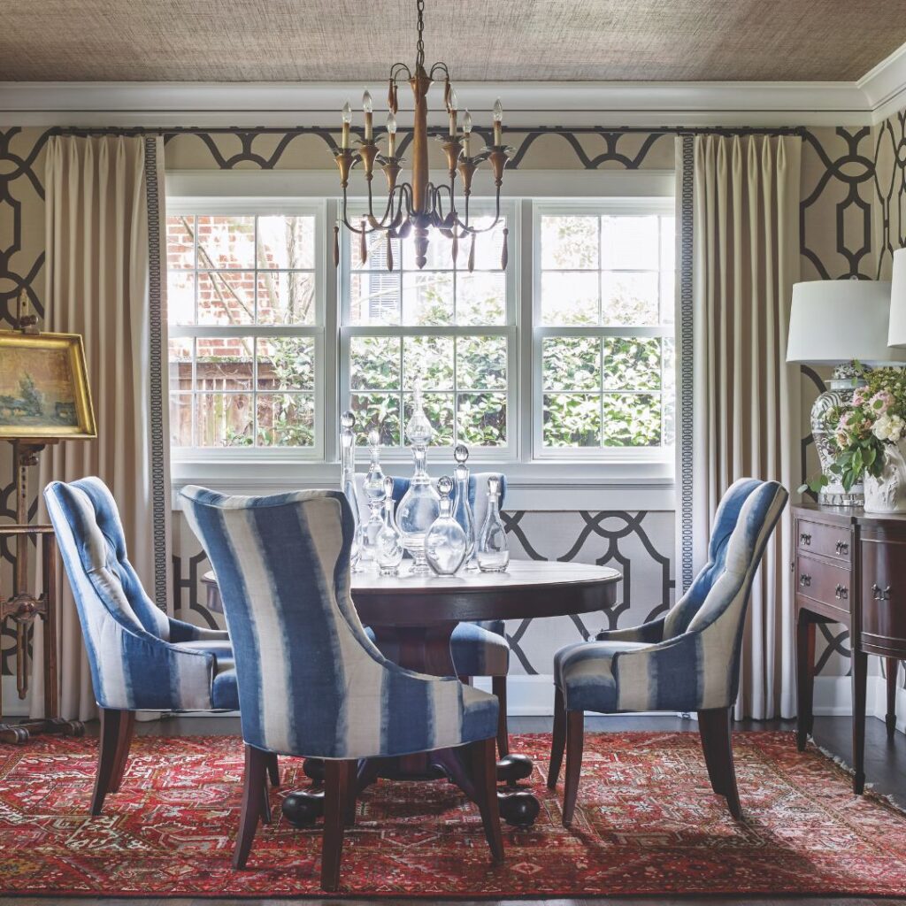 A formal dining room with trellis wallpaper and blue-and-white striped chairs