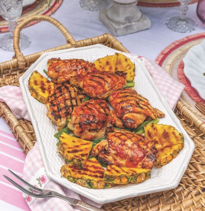 Pineapple Chicken Thighs on a white platter and wicker tray