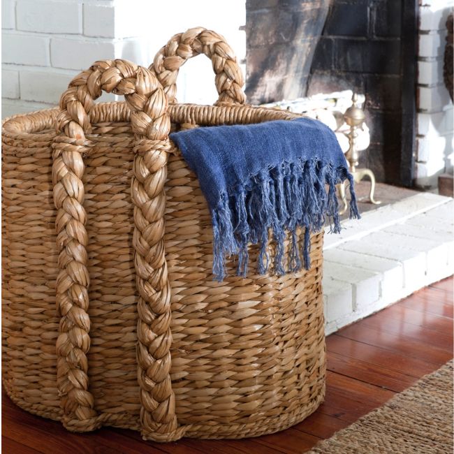 Large basket draped with a blue blanket by a fireplace