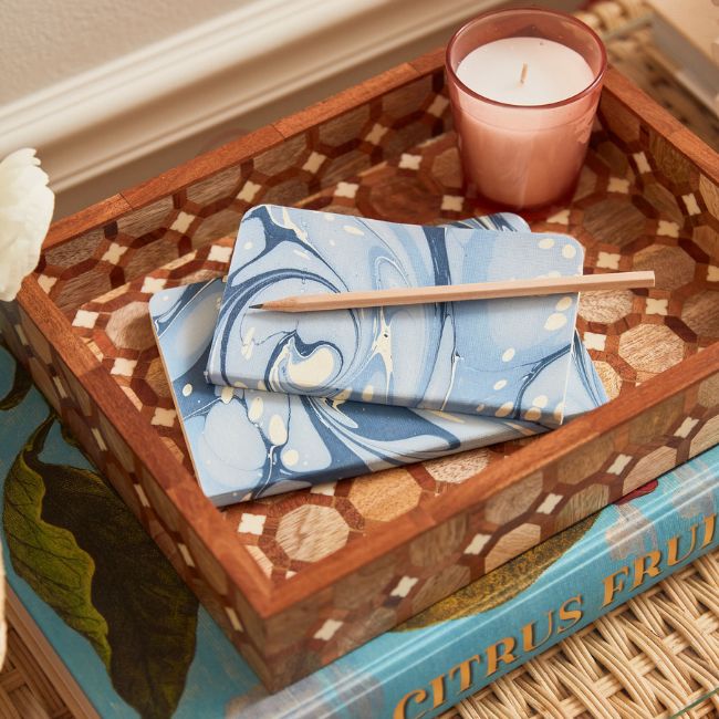 A small wooden tray holding notepads, a pencil, and a candle