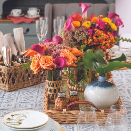 Hot pink and orange florals in vases atop a woven serving tray