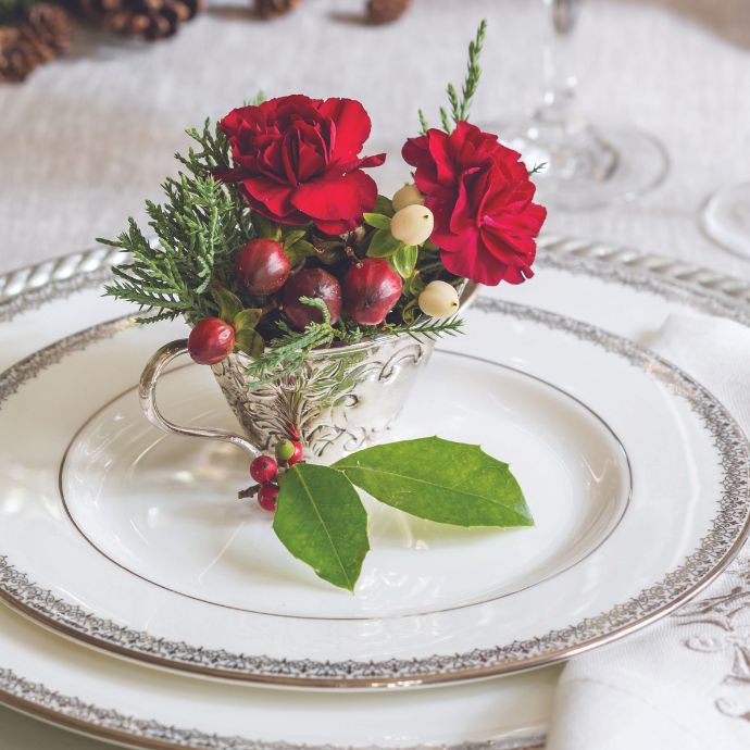 Flowers and berries in a silver cup atop a place setting