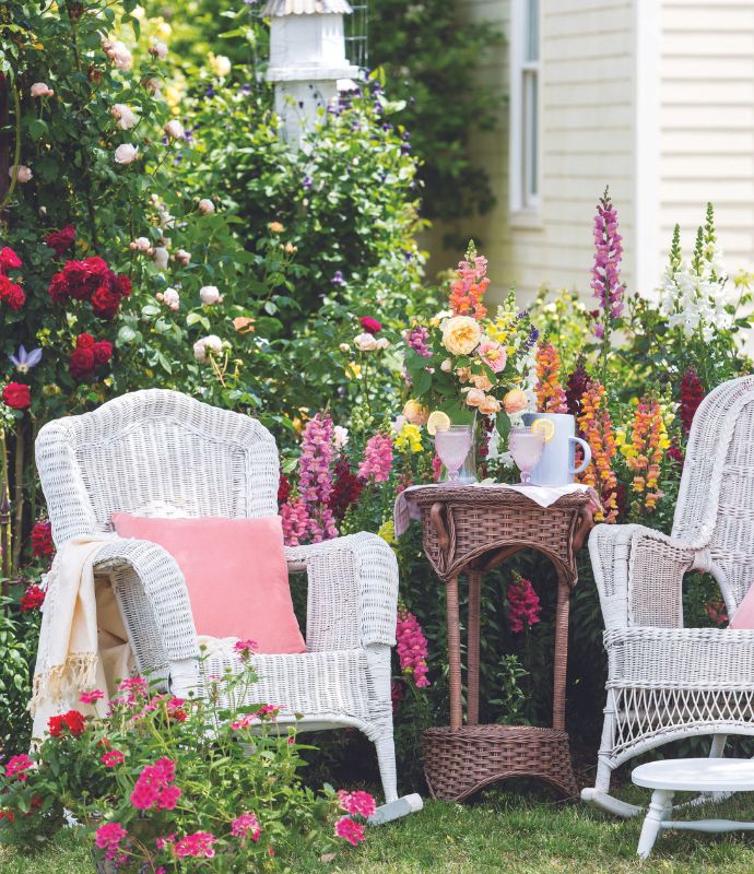 Two white wicker chairs and a table set with refreshments in a garden