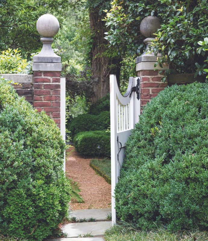 Brick columns and a white gate open to a green garden room