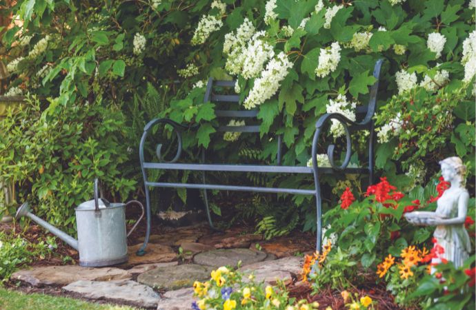 An iron garden bench framed by statuary and a watering can