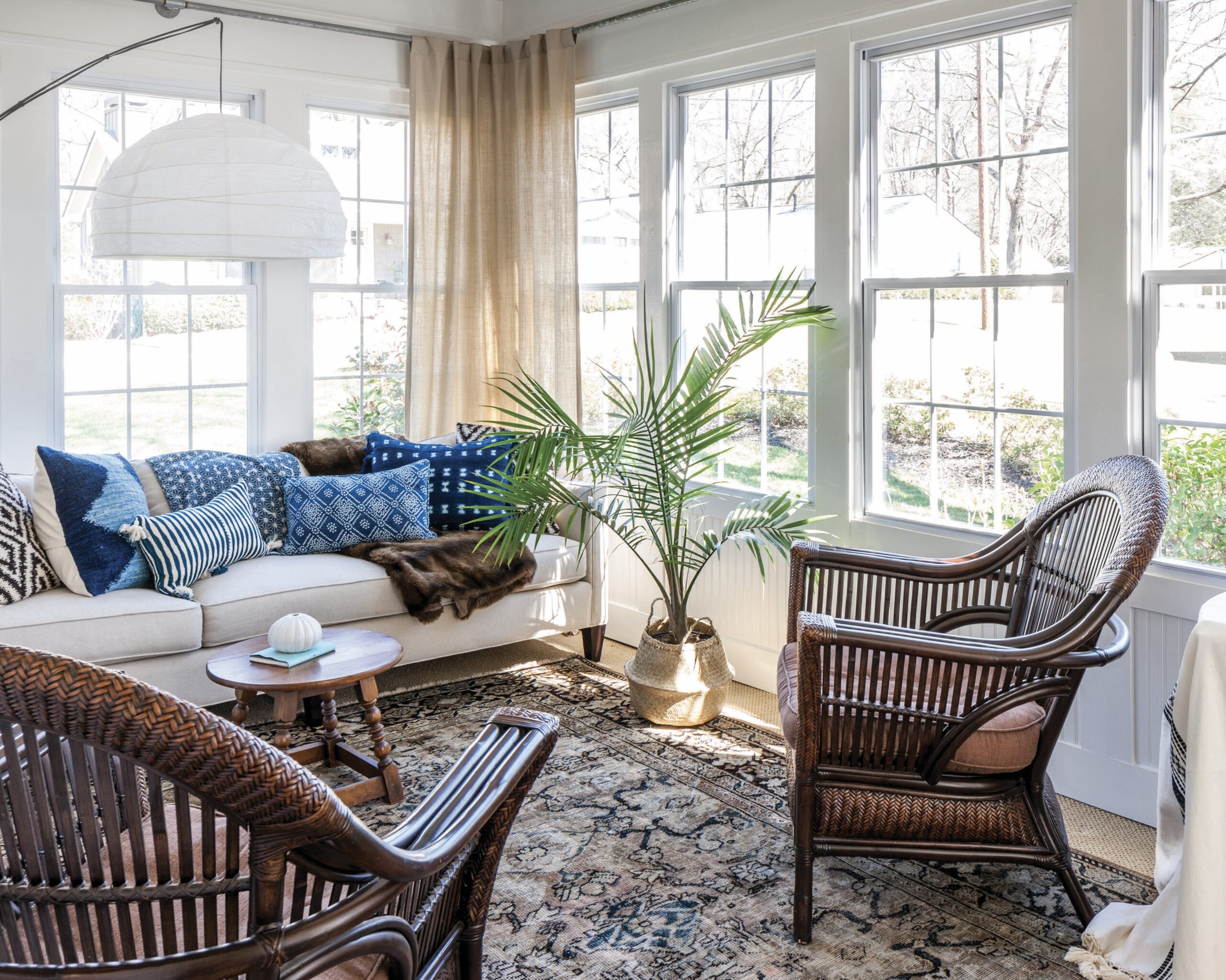 A sunroom with dark wicker furniture and blue pillows