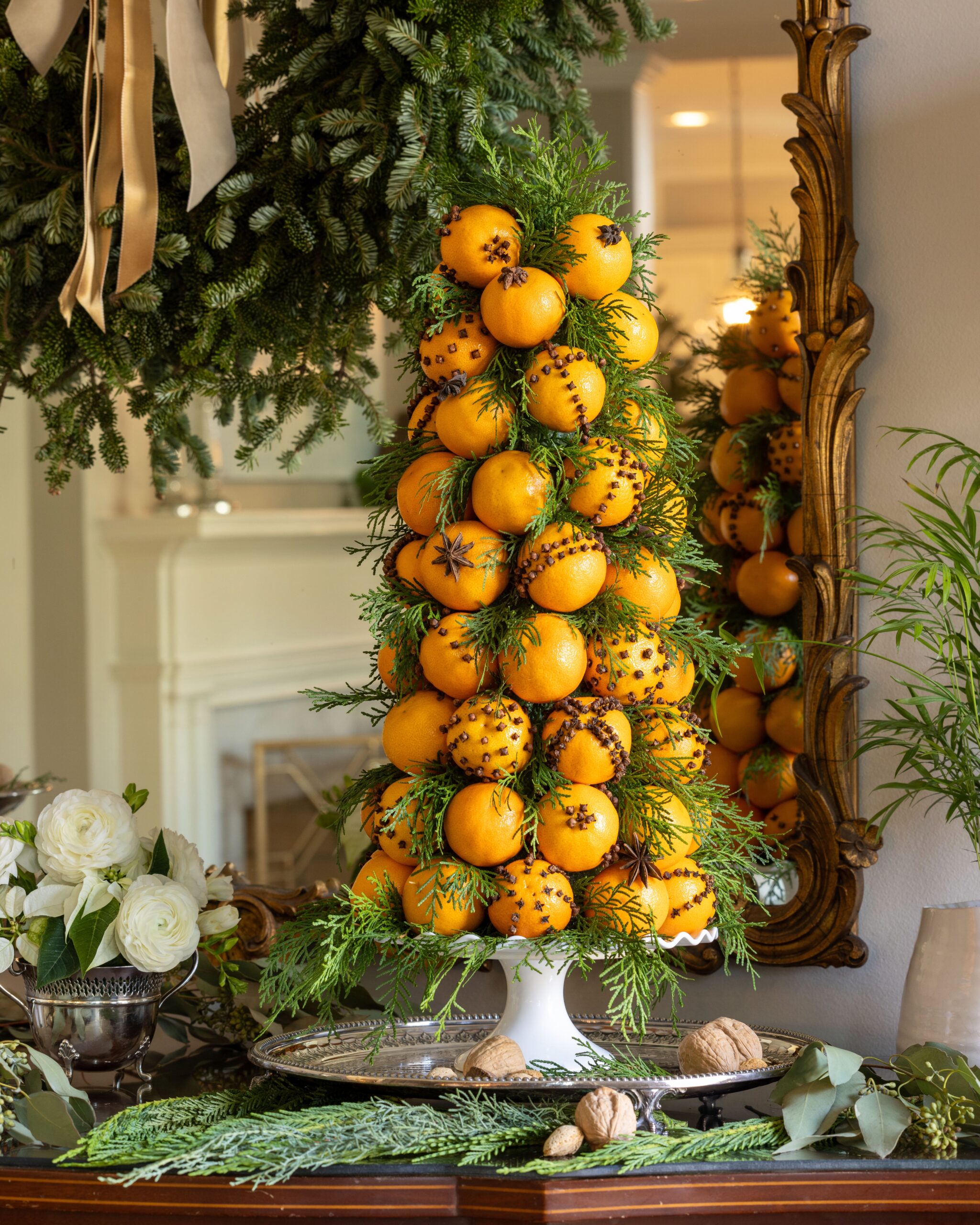 A topiary Christmas tree made from pomander oranges studded with cloves and greenery, on a buffet table in a formal dining room decked for the holidays
