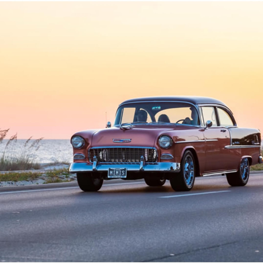 A red 1955 Chevrolet Bel Air drives along the shore of a Mississippi beach at sunset during the festival Cruisin' the Coast.