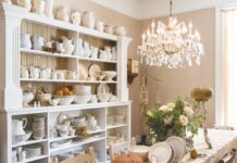 In Love with White Ironstone China An extensive collection of white ironstone china dishware, including plates, pitchers, cups, and vases, sits on a white hutch in a dining room with a chandelier.