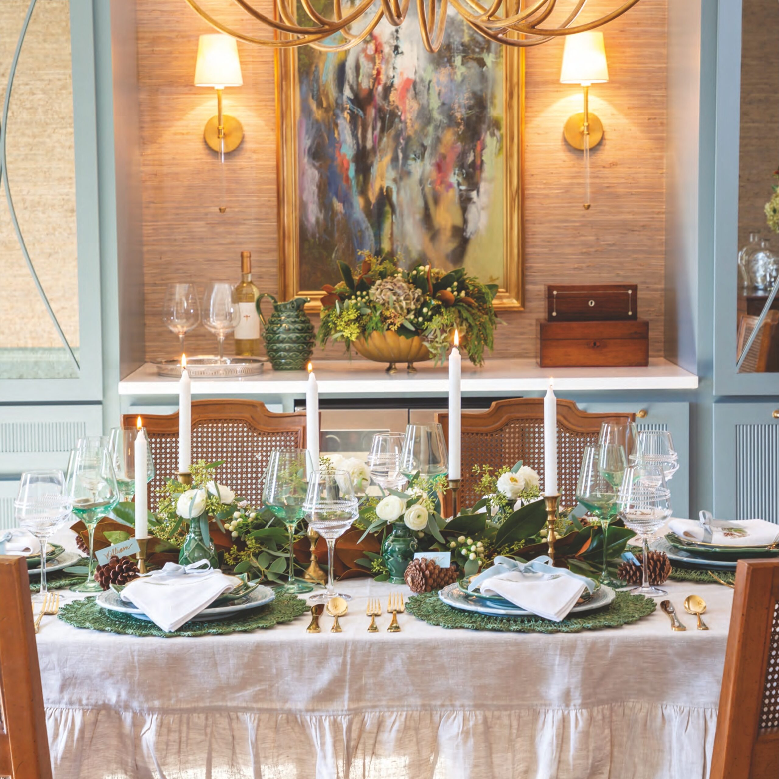 A Christmas place setting with green and blue place settings, taper candles, and a white linen ruffled tablecloth in a formal dining room.