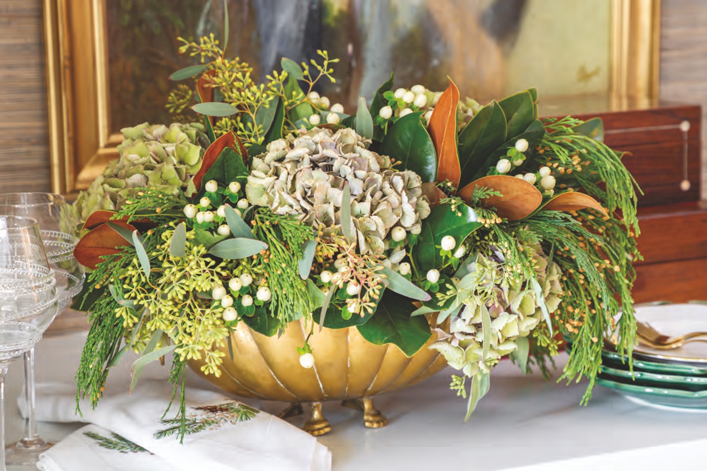 A low centerpiece of evergreen magnolia leaves, seeded eucalyptus, and brunia berries interwoven with vases of snow-white ranunculus.