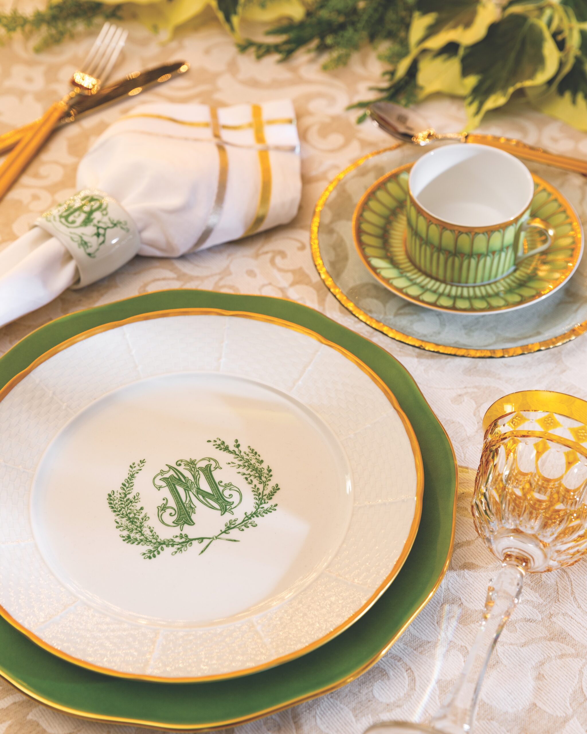 Bearing wreath-inspired monograms, a pristine white plate and napkin ring by Sasha Nichols anchor an arrangement fit for any December fete. Variegated shades of green on the cup-and-saucer set, along with a fern-hued charger, play off the entwined initials