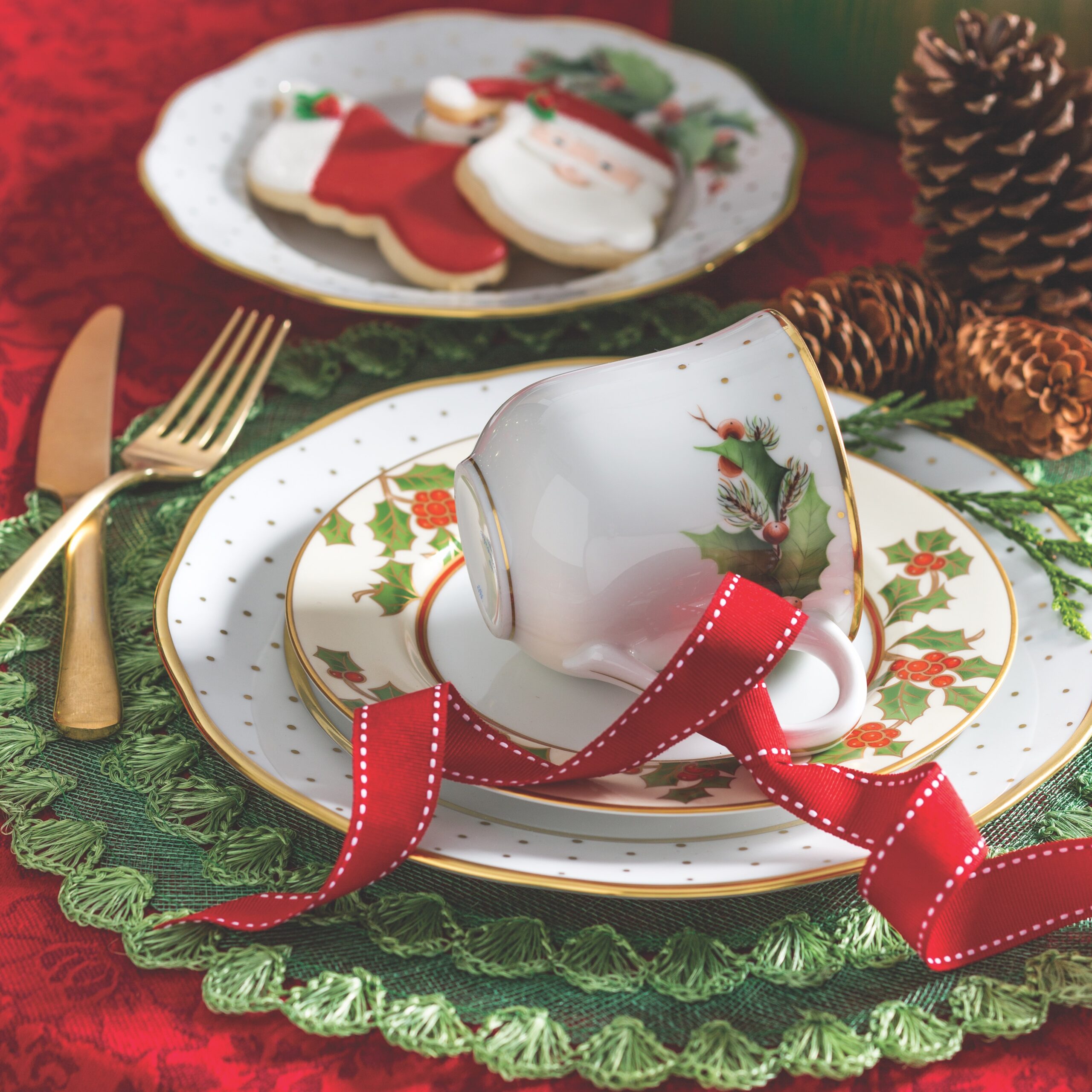 A flamboyant red tablecloth highlights the bright berries of two wintertime collections. Herend's Winter Shimmer teacup and Fitz and Floyd's Christmas Holly dessert plate are idyllic companions layered on a polka-dot dish. The delicately woven place mat sprigs of cedar, and foraged pine cones add textural interest.