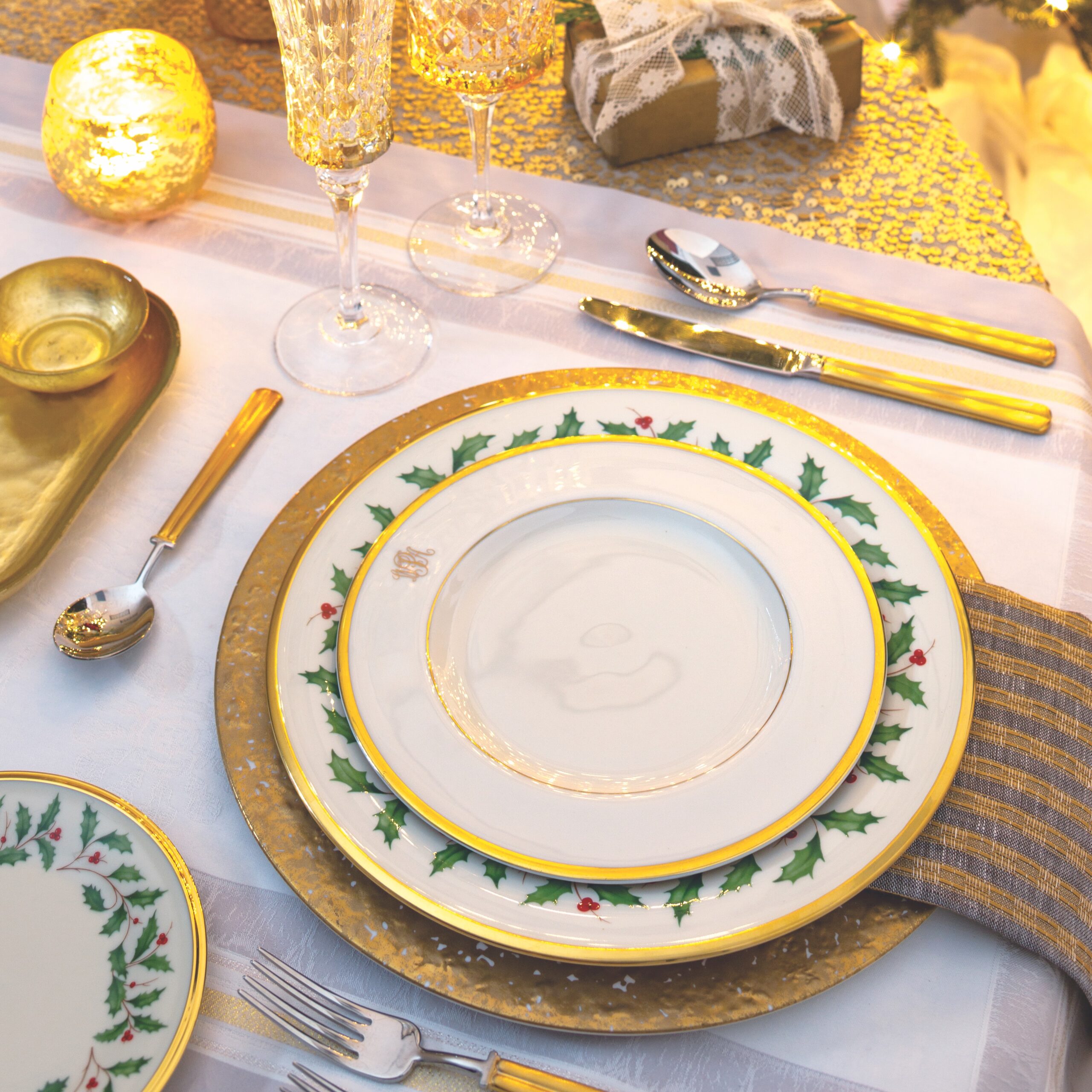 A gold-and-green place setting consisting of Lenox's Holiday dinner plate, a gold charger, goblets, gold flatware, and a napkin with metallic stripes.