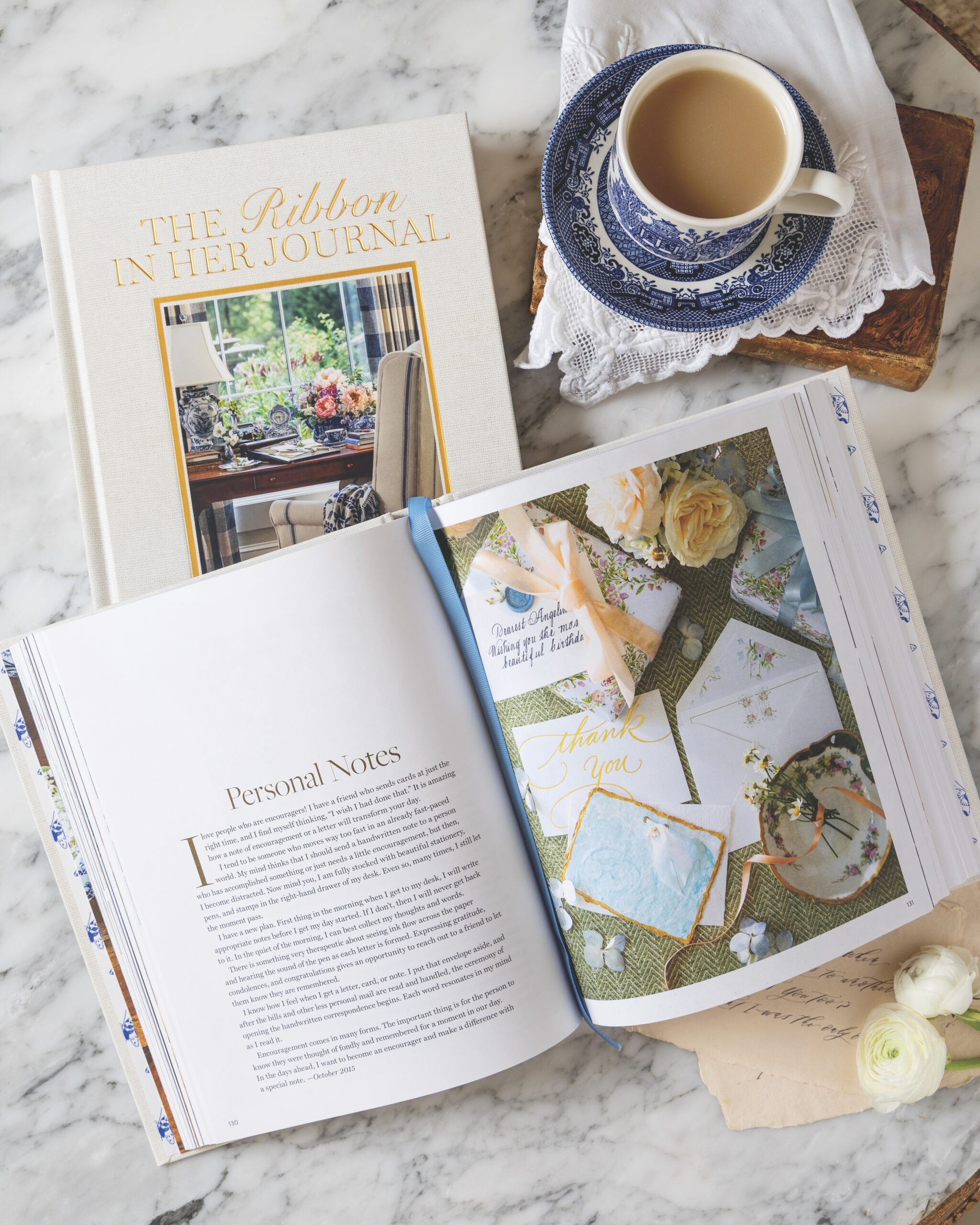The Ribbon In Her Journal book open to a pretty page, with a cup of tea.
