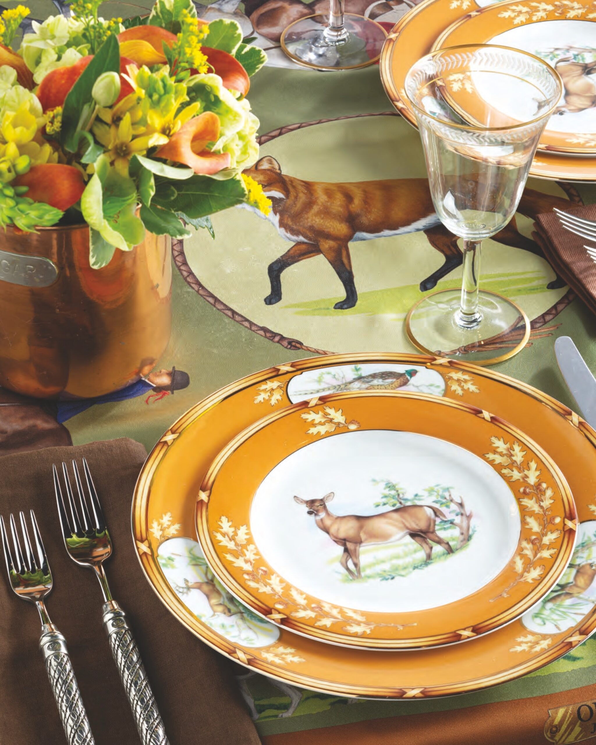 Julie Wear’s American Wildlife plates in a place setting, with a goblet and silver flatware.