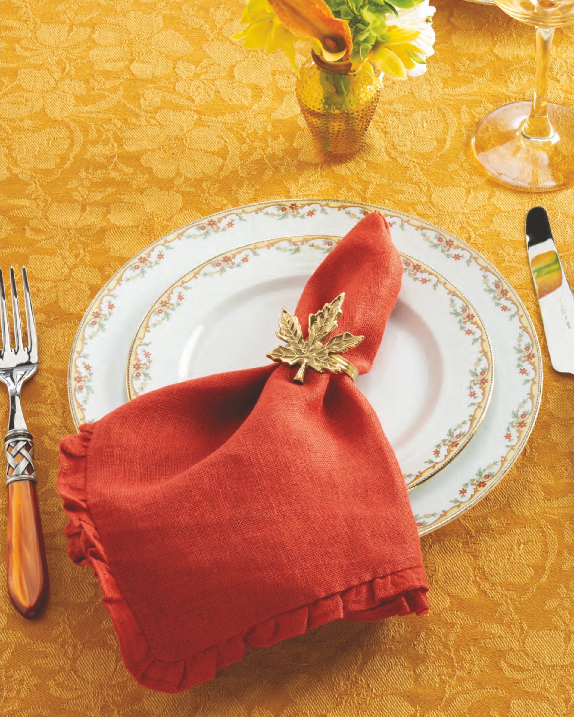 The Meuse by Vignaud plates in a place setting with an orange napkin tucked in a leaf ring.