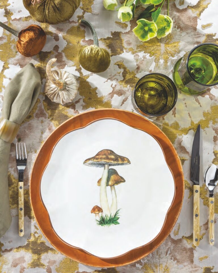 A Scalloped Mushroom dinner plate by Mrs. Alice atop a brown plate, with velveteen pumpkins and a swath of leafy green linens and glassware.