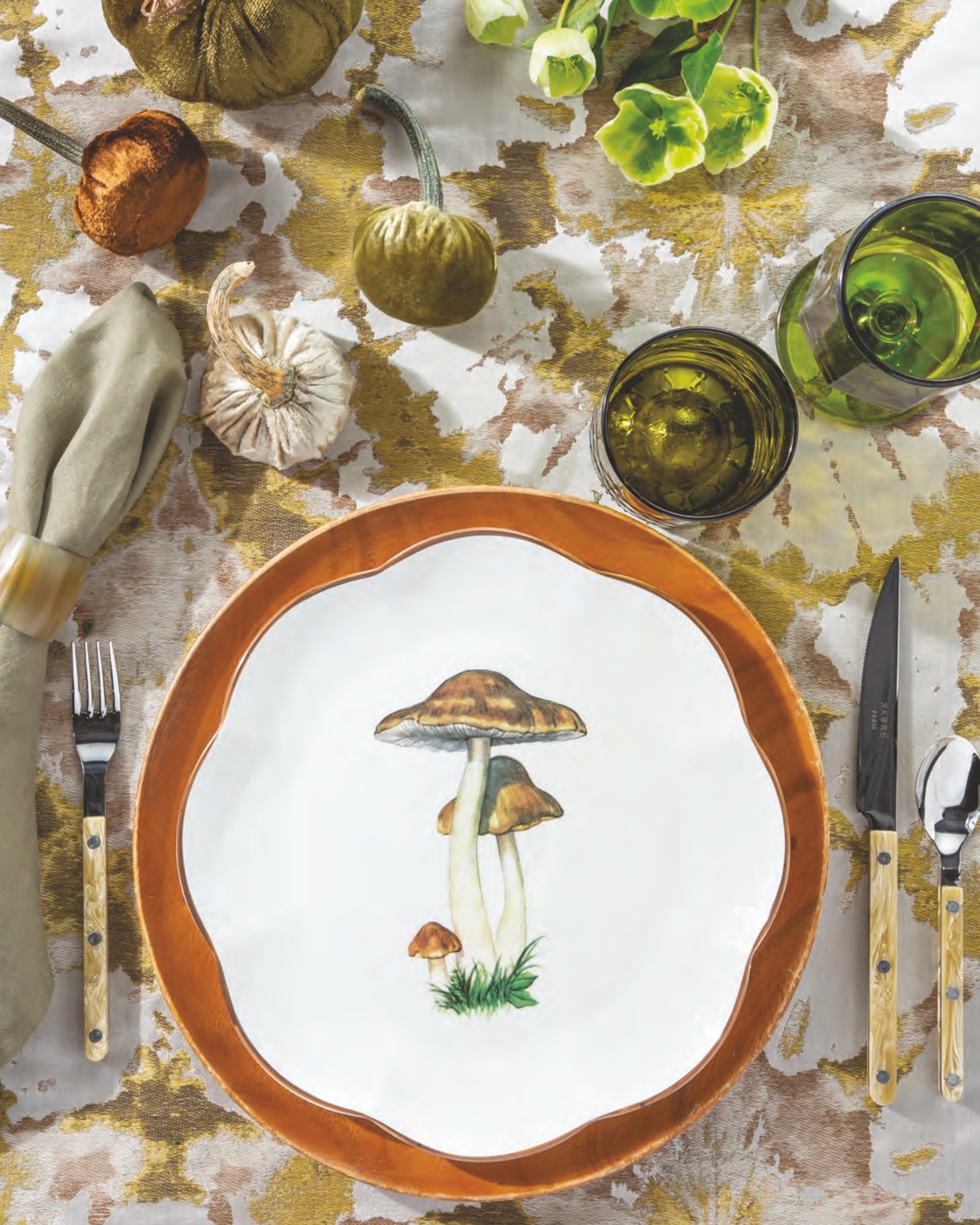 A Scalloped Mushroom dinner plate by Mrs. Alice atop a brown plate, with velveteen pumpkins and a swath of leafy green linens and glassware.