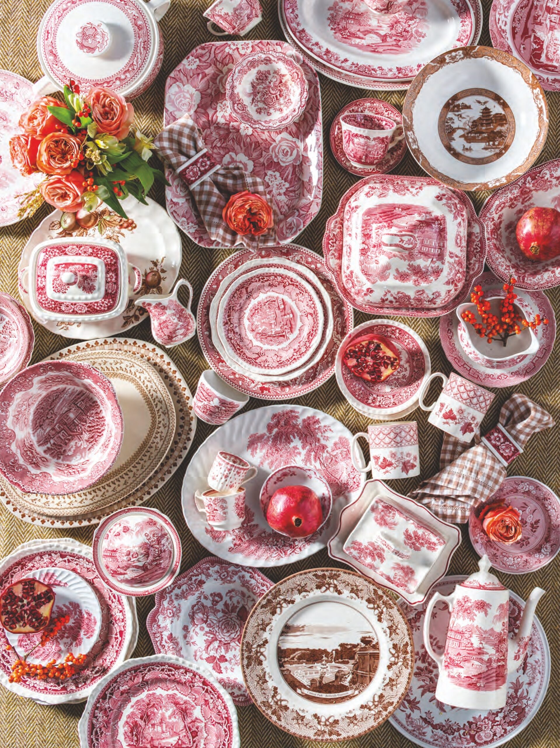 A flatlay of red and brown transferware plates, butter pats, casserole dishes, and tea cups with flowers.