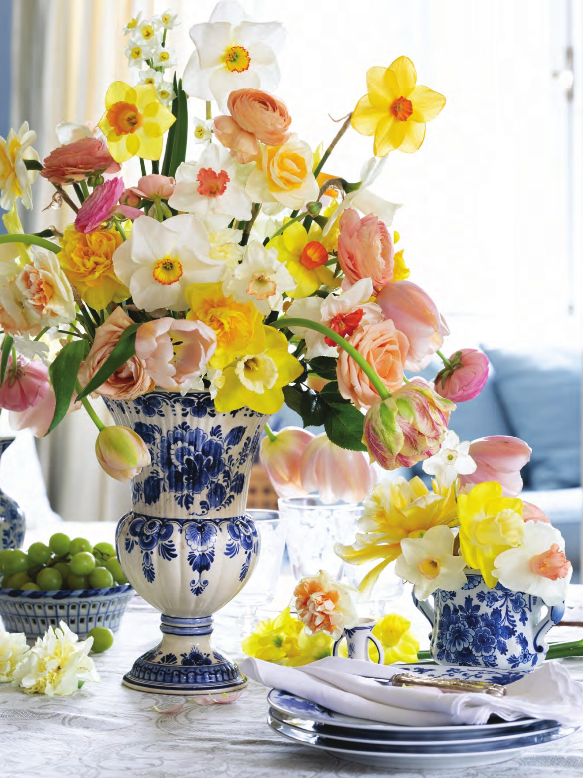 Bountiful spring flower arrangements of daffodils, tulips, roses, and more, in blue and white vases.