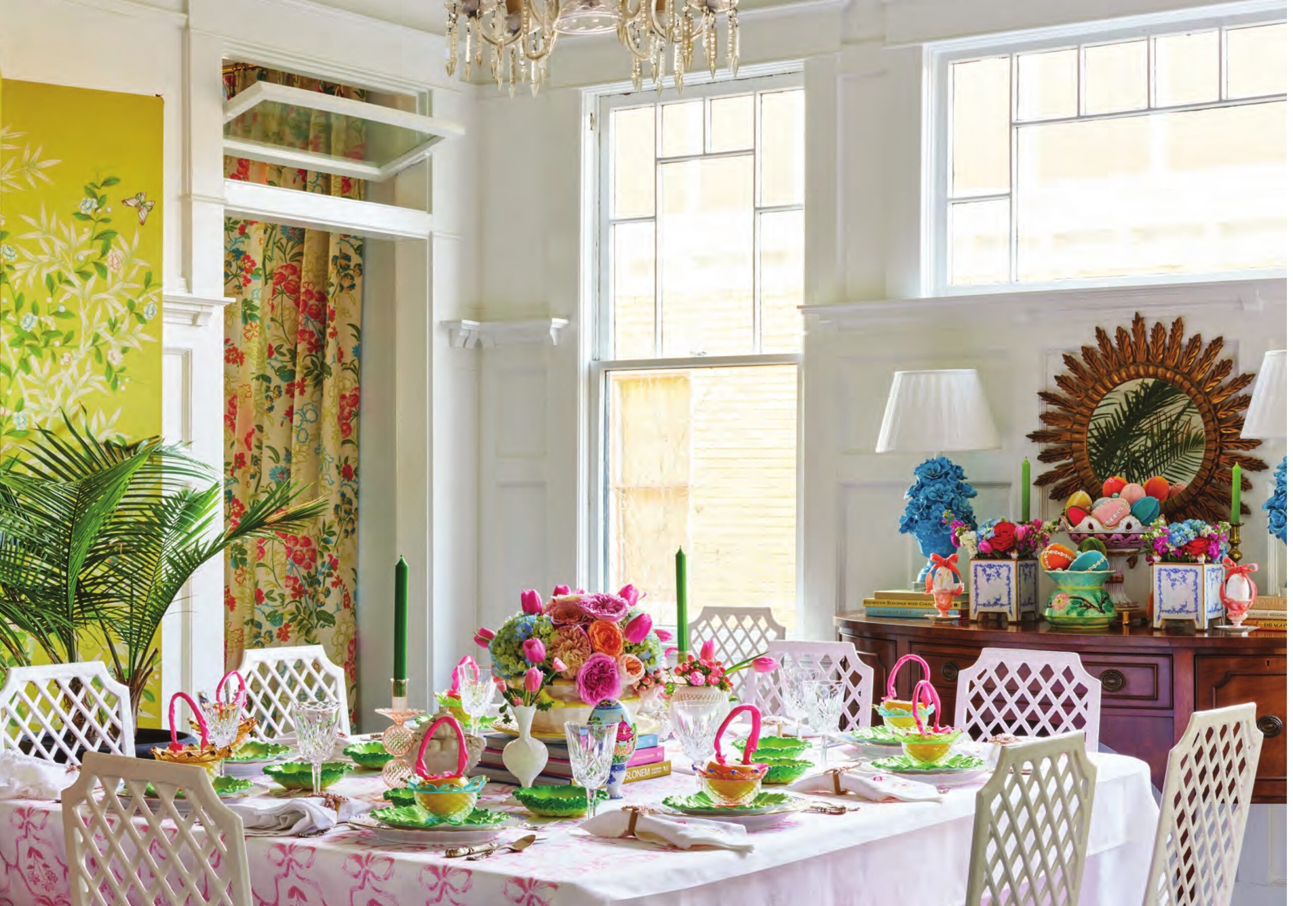 A colorful Easter tablescape in Lydia Menzie's dining room, featuring yellow floral wallpaper, a pink-and-green tablescape, pink floral tablecloth, and white trellis-back chairs.