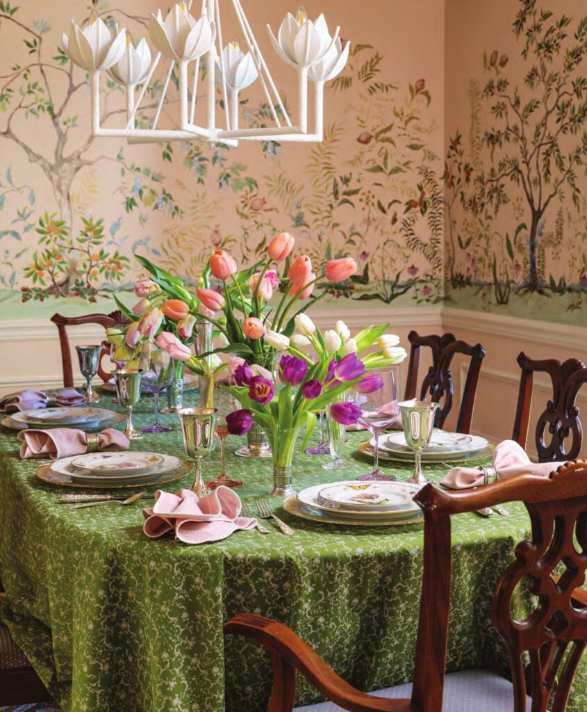 A spring tablescape with tulips, in a dining room adorned with a mural floral wallpaper.