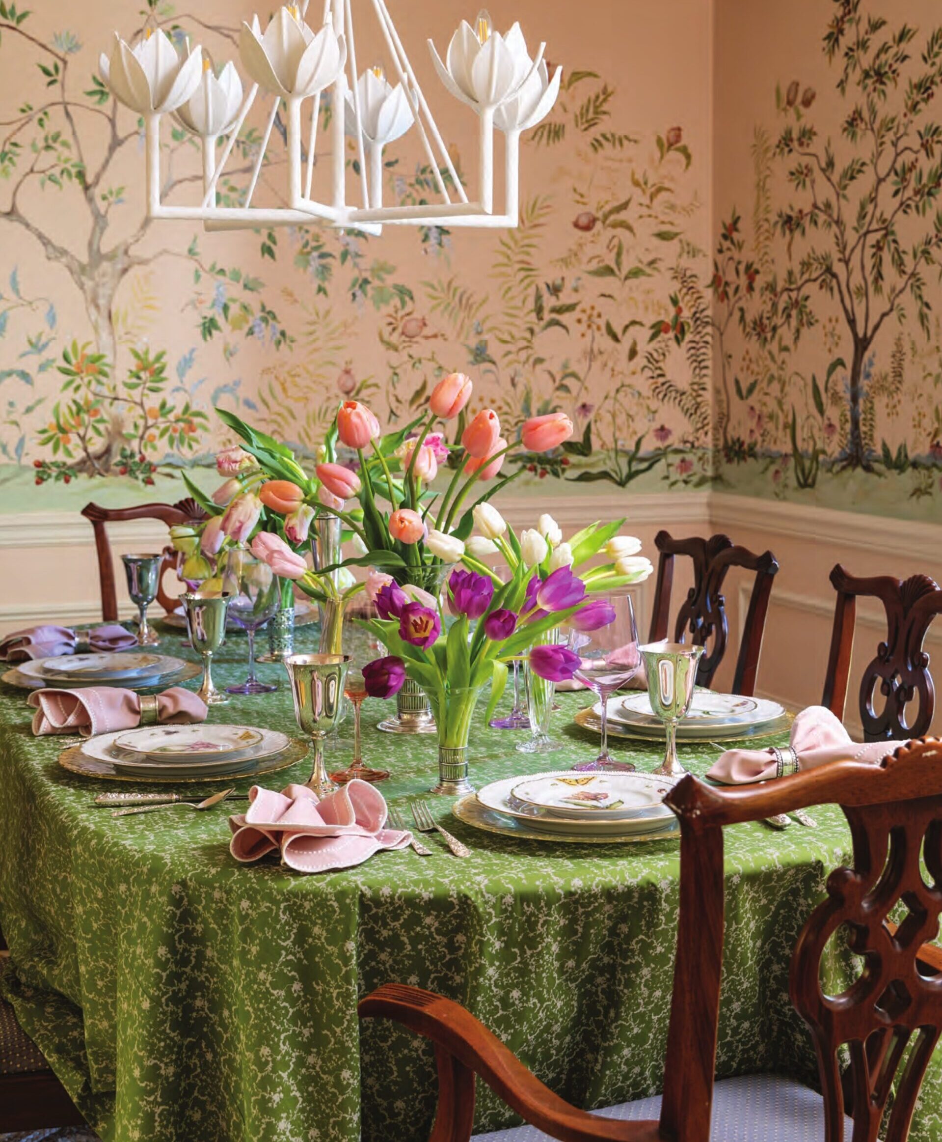 A spring tablescape with tulips, in a dining room adorned with a mural floral wallpaper.