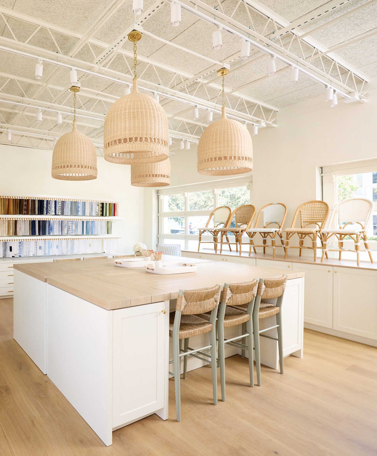 A design studio workspace in the Serena and Lily store, with pendant lights, an expansive work table, and bistro chairs.