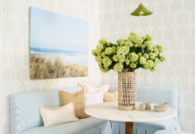 Step Inside Serena & Lily’s Coastal Design Destination in Naples A cozy nook with light blue bench seating, including a pleated skirt, a beachy landscape art piece, and a table with an abundant hydrangea arrangement.